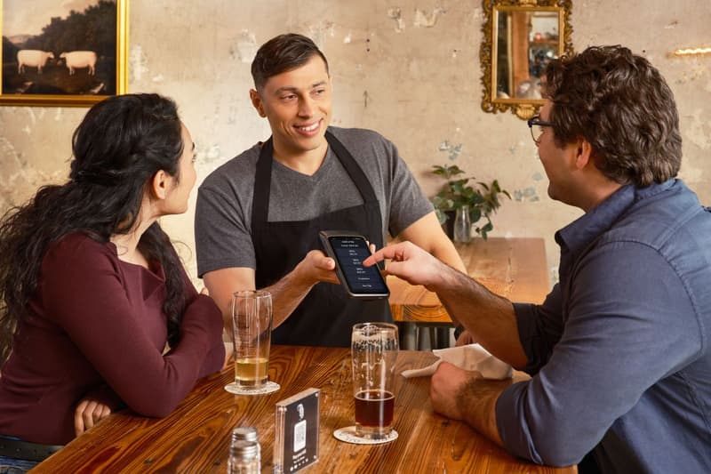 Mozo mostrando un pedido en el celular a comensales en la mesa de un restaurante